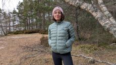 A woman on a beach wearing a green down jacket with hands in pockets