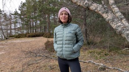 A woman on a beach wearing a green down jacket with hands in pockets