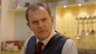 Hugh Bonneville sits at the kitchen table looking confused in Paddington 2.