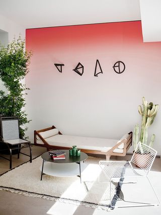 A coffee table with two chairs and a day bed in front of a wall painted in a red ombre effect with four black 3D models