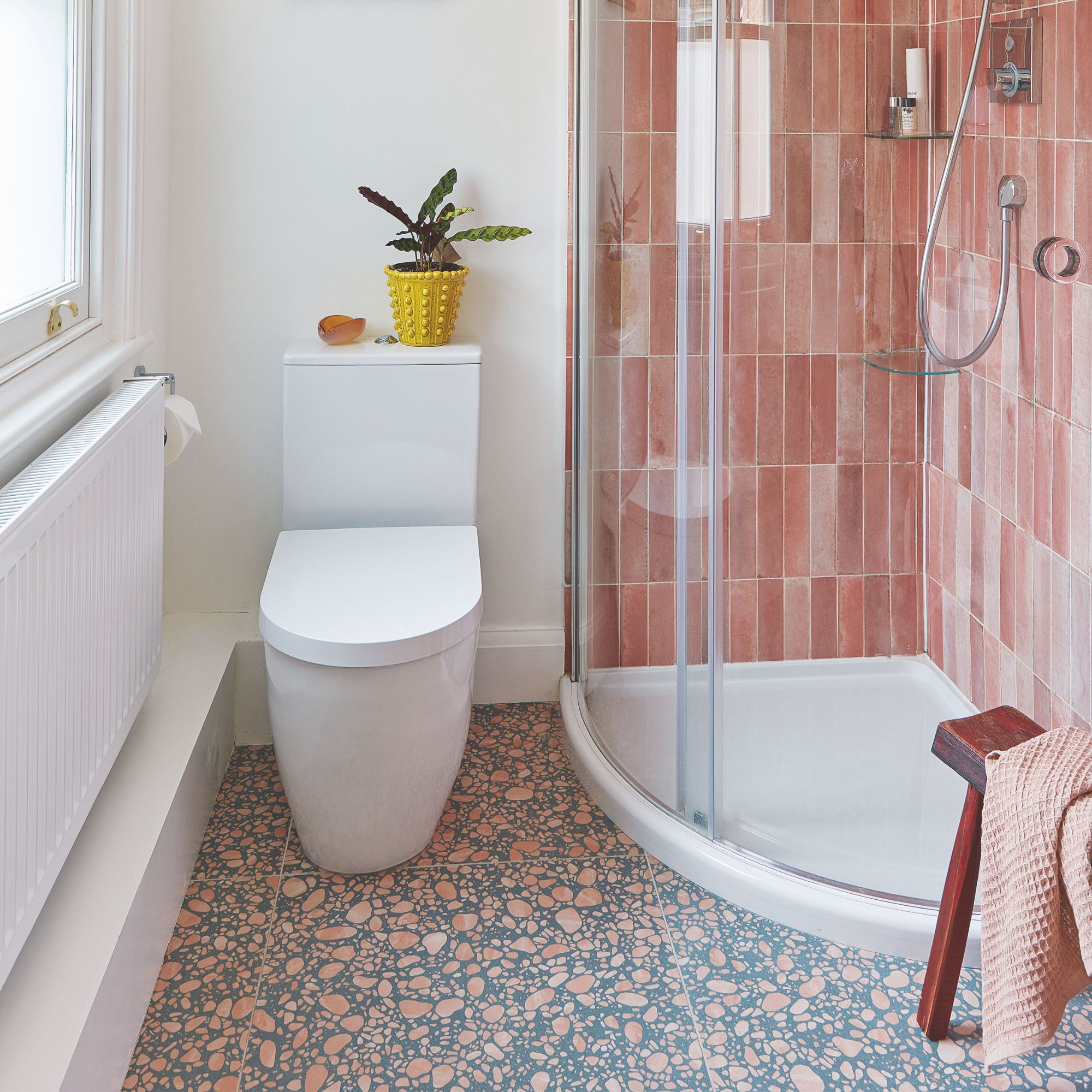 White painted bathroom with white toilet and white shower tray with pink shower tiles around it