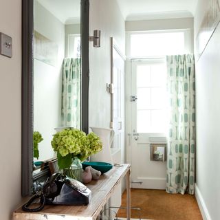 A white hallway with a large mirror, side table and green patterned door curtain