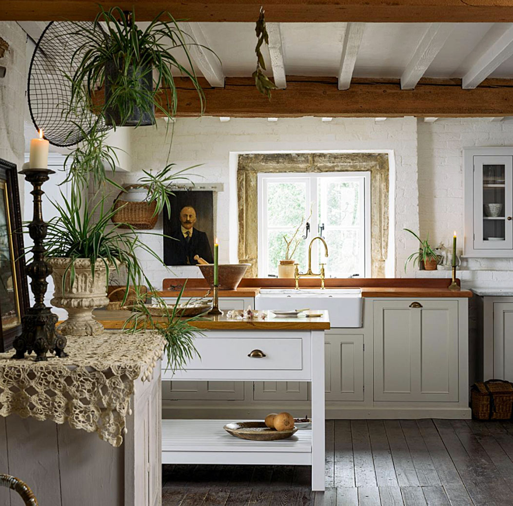 A country style kitchen with white painted beams, a small white central island and green palm plants