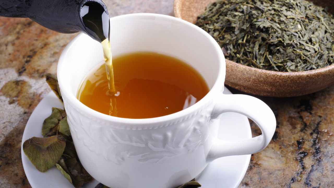 Tea pouring into a teacup next to a bowl of dried herbs