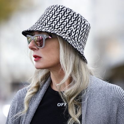 Best lipsticks for older women - Petra van Bremen wearing a black and white bucket hat by Valentino, a black t-shirt by Off-White, black shorts with belt by Off-White, a long silver knitted coat by Balenciaga, transparent frame sunglasses by Westward Leaning, - gettyimages1355367186
