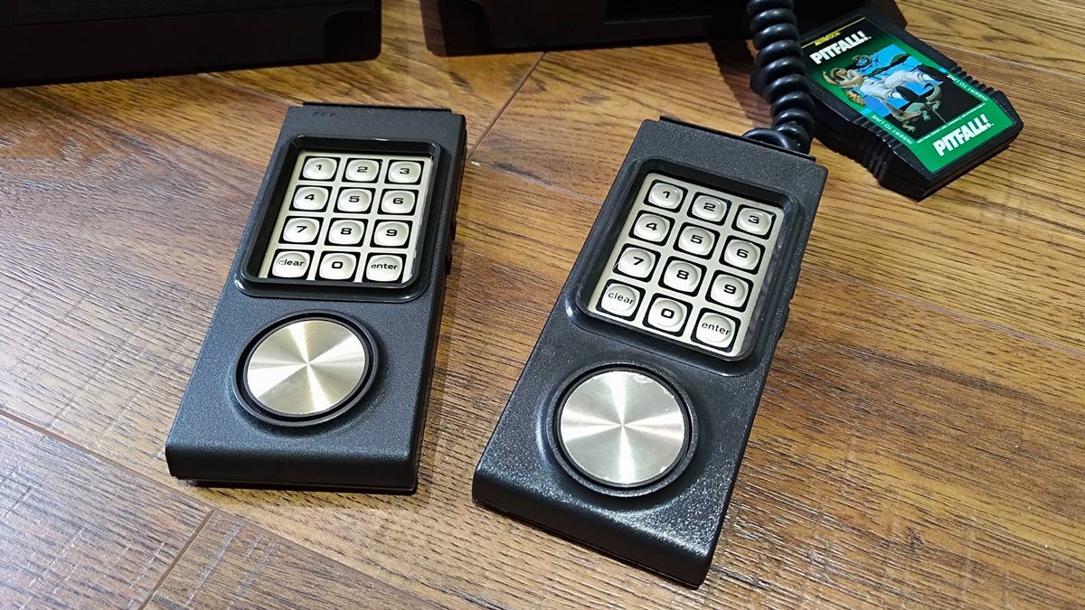 Intellivision Sprint controller next to original wired gamepad on woodgrain floor