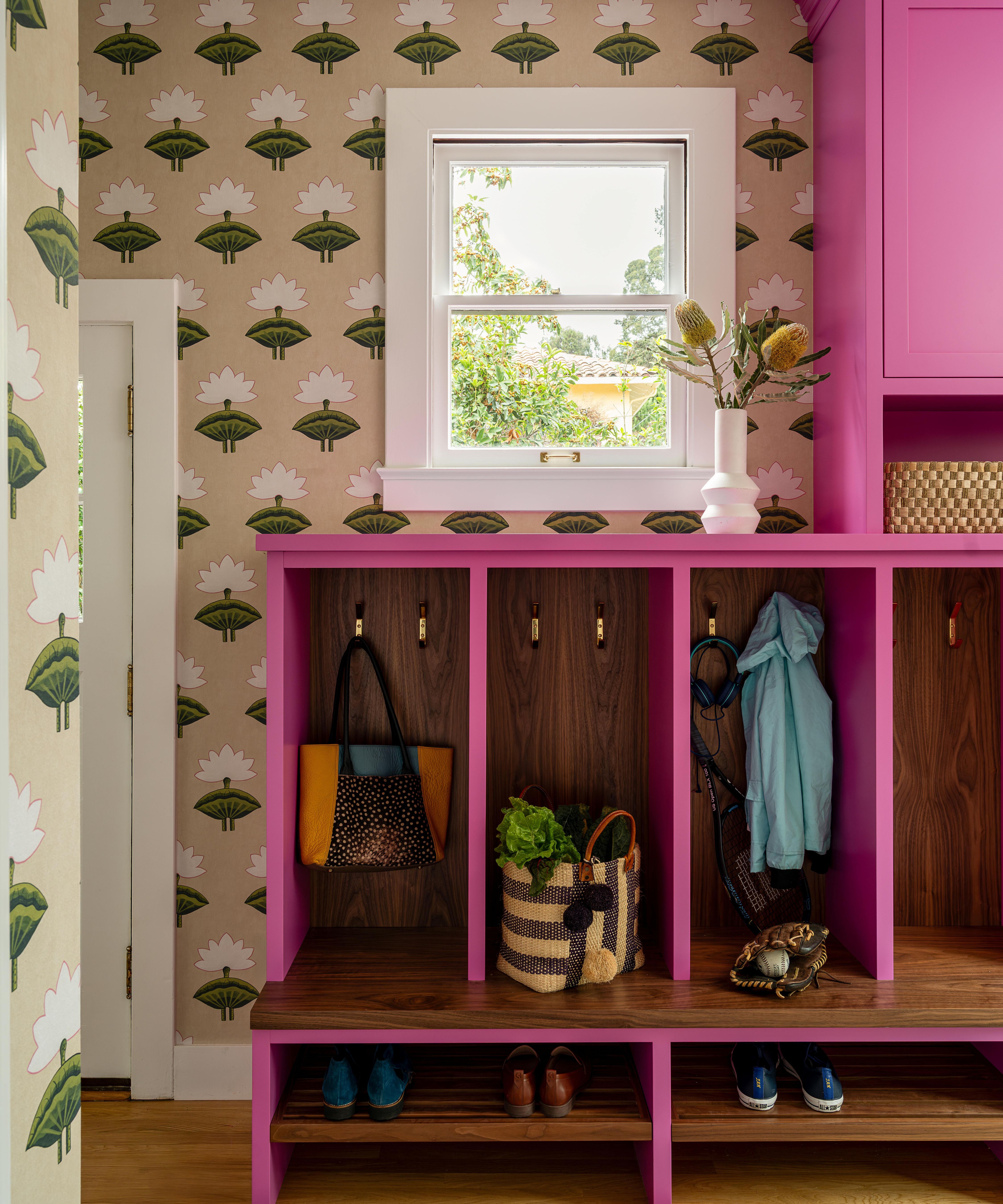 a floral wallpapered mudroom with vibrant pink cabinetry with hooks for shoes and coats