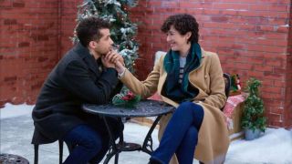 Max holding Alice's hand to his chin while sitting at a patio table in the snow.