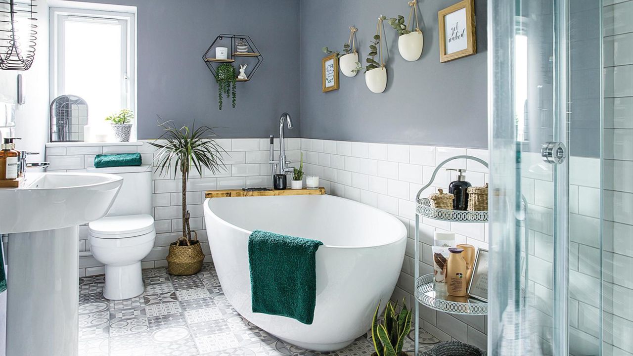 bathroom with white freestanding bath, white toilet and basin, green potted plant, white and grey floor tiles, white wall tiles and grey walls 