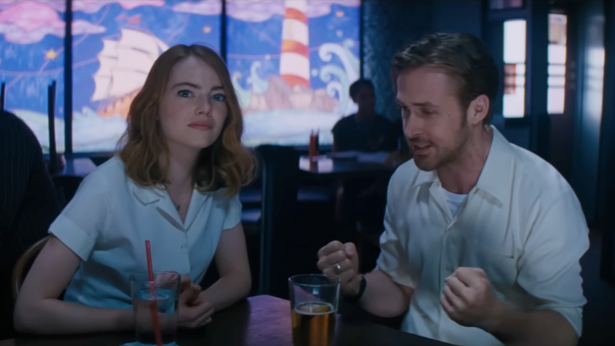 Emma Stone looking forward and Ryan Gosling looking down and passionate while his hands are in fists in La La Land. 
