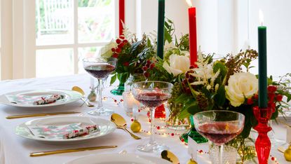 traditional Christmas colors on a dining table with taper candles, foliage and wine glasses