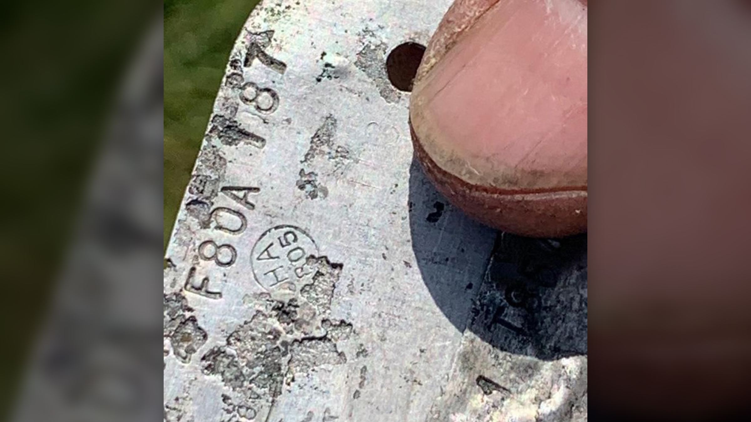 We see a person's thumb over a metal piece that has imprinted numbers and letters.