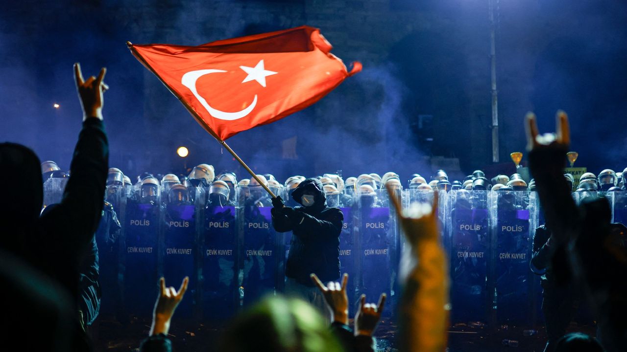 A protester waves Turkey&#039;s national flag before Turkish riot police as protesters flash the grey-wolf salute during a demonstration outside Istanbul&#039;s city hall to support Istanbul mayor Ekrem Imamoglu following his arrest 