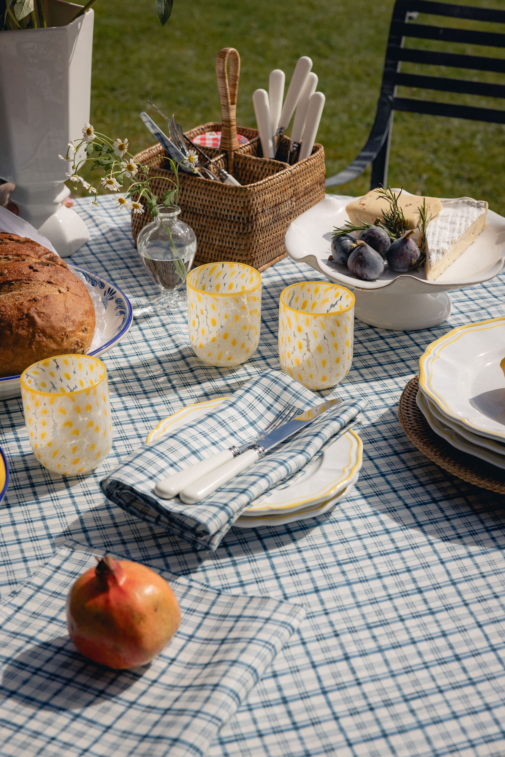 Close-up of an outdoor table set with a blue and white plaid tablecloth, yellow glassware and plates, matching napkins, and wicker serving baskets.