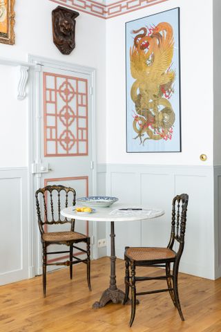Corner of a dining room with bistro set, pale blue door and panelling, and pink decorative detailing and frieze