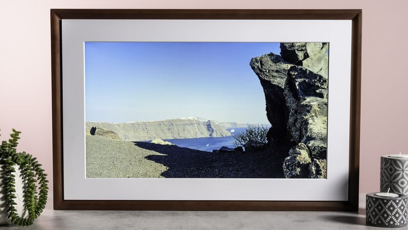 The Netgear Meural Canvas II showing a photo of rocky cliffs and an azure sea. It&#039;s surrounded by a plant and some patterned candle holders.