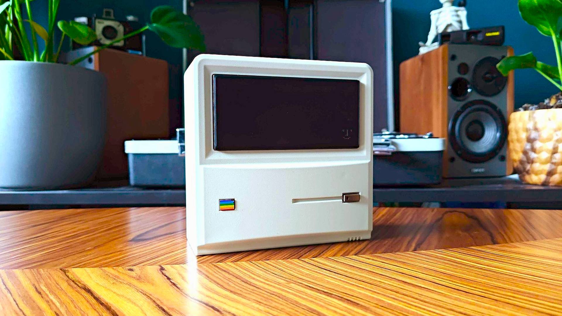 Ayaneo Mini PC AM01 on woodgrain table with plants and speakers in backdrop.