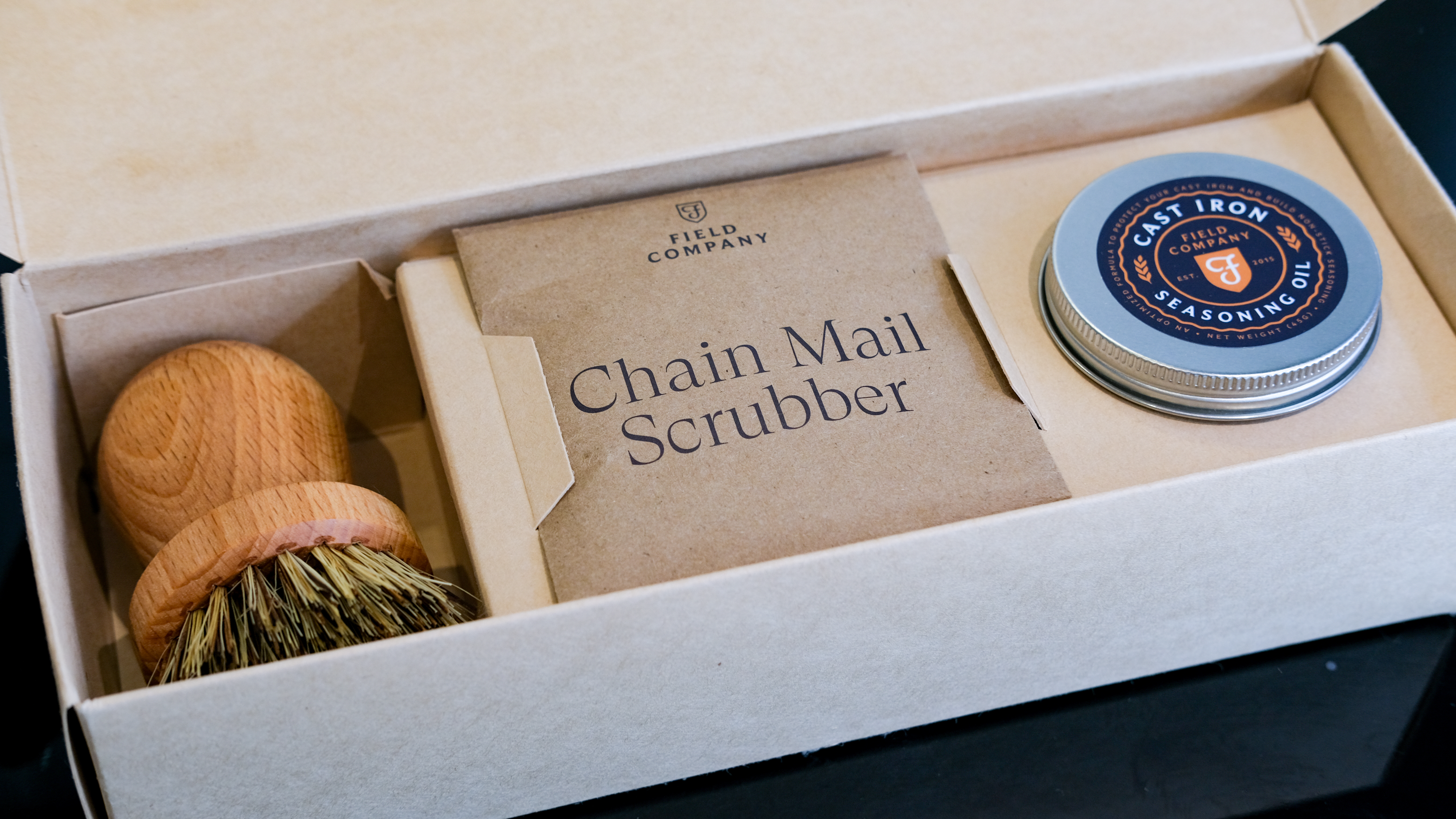 The Field Company Skillet care and cleaning set open, showing a brush, chainmail scourer and a pot of cast iron seasoning oil