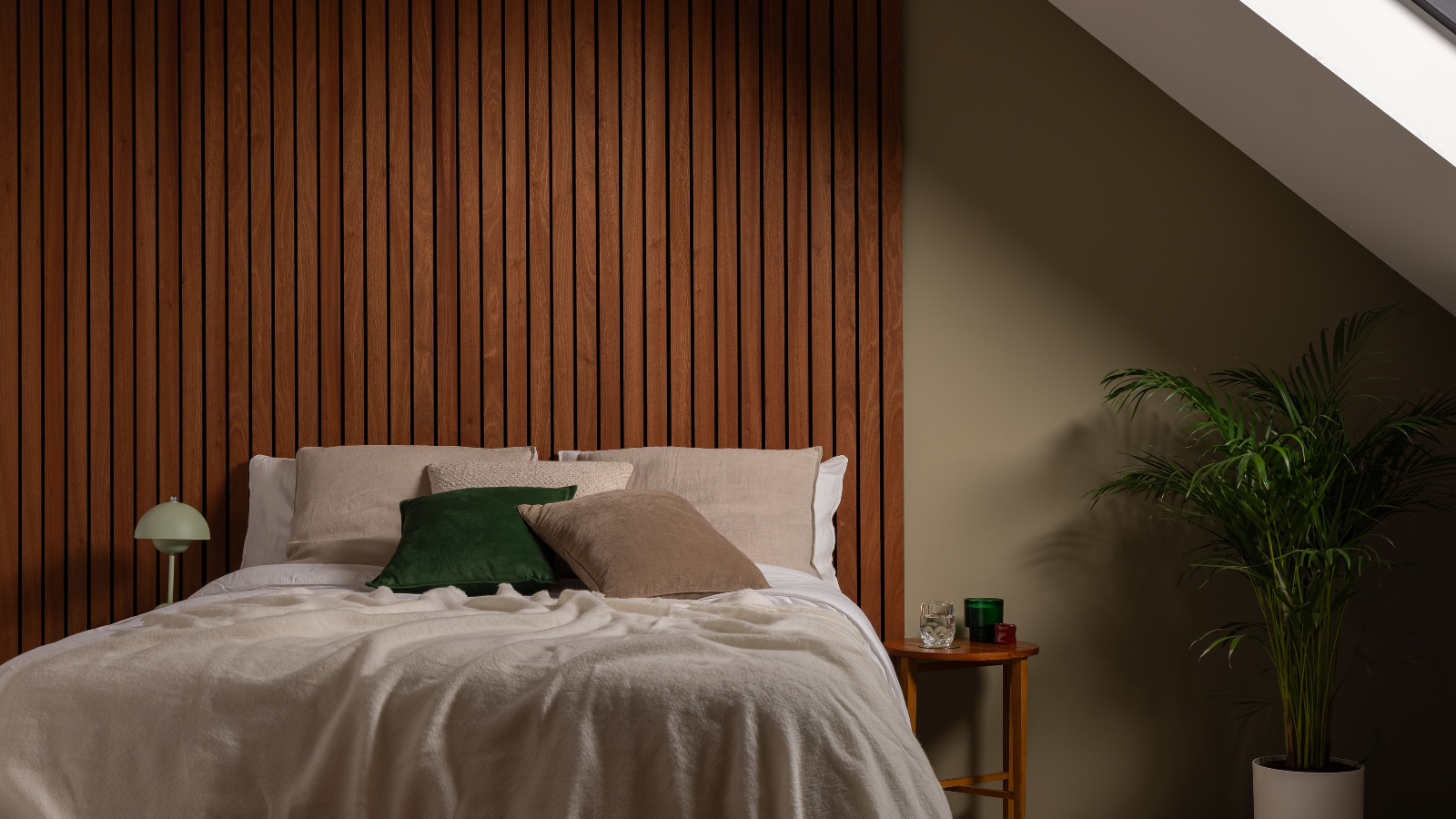 Bedroom with dark wooden panelling behind the bed, a green wall, a plant in the corner, and beige and green decorative elements