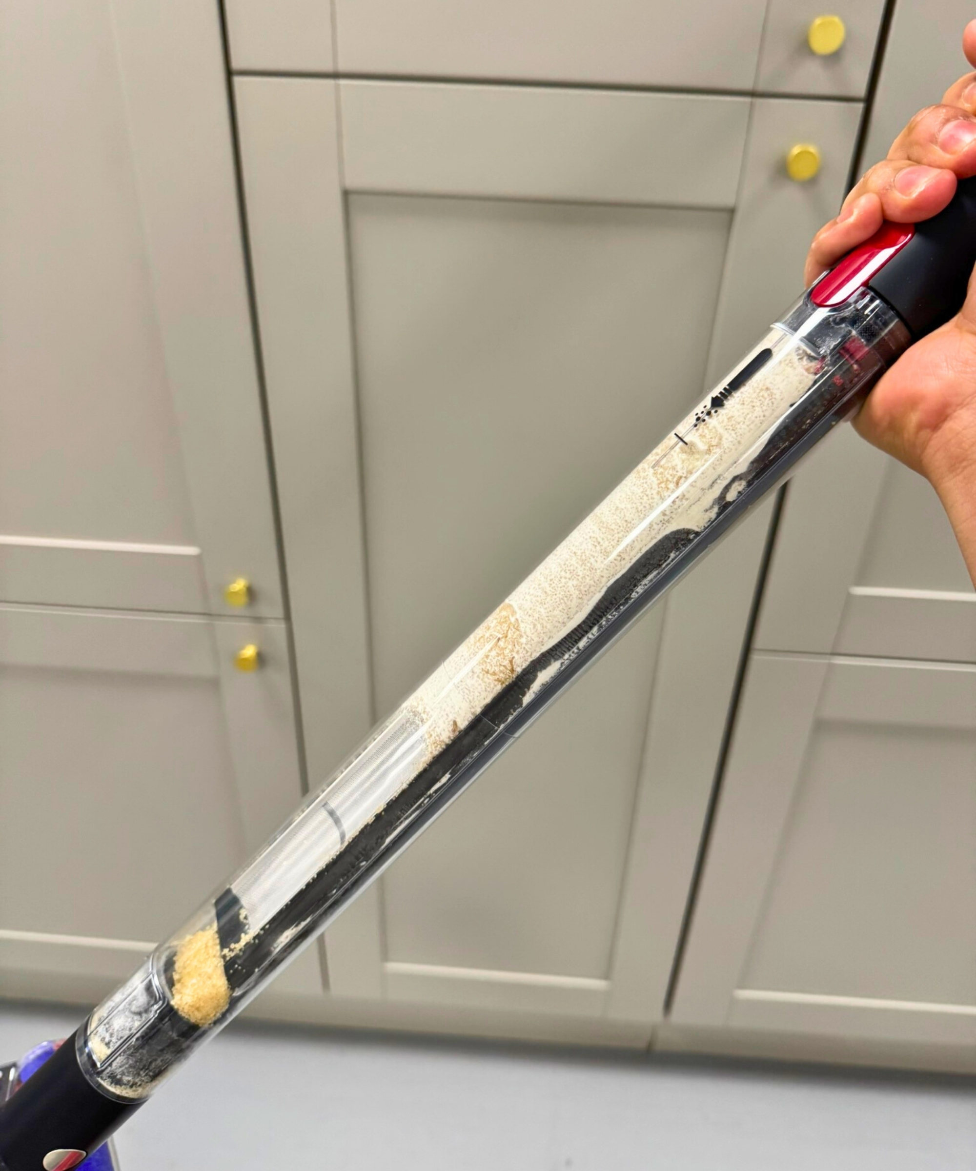 Hand holding the Dyson PencilVac Fluffycones showing the dustbin that is half full of dust and dirt.