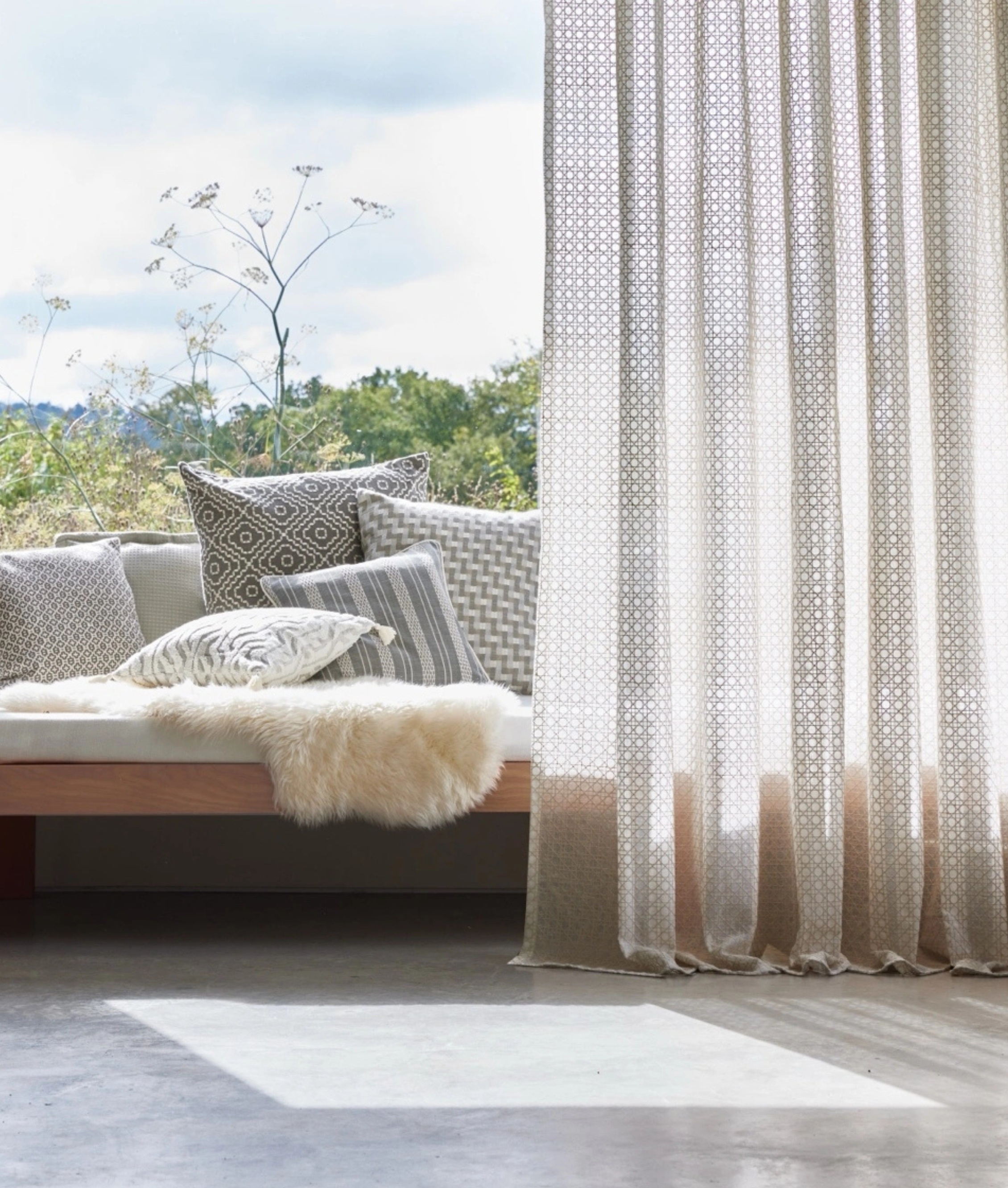 a window seat in a modern home with cushions and a sheer curtain