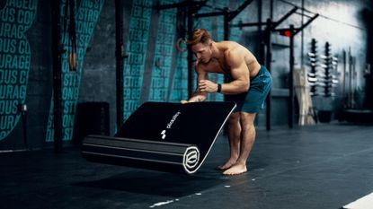 Athlete Noah Ohlsen unrolling a yoga mat 