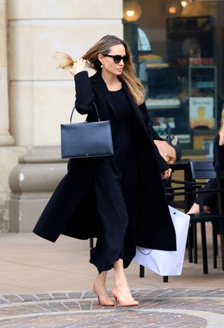 Angelina Jolie wears a black coat and black dress with nude heels.