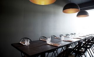 A restaurant with long table chairs and statement lights