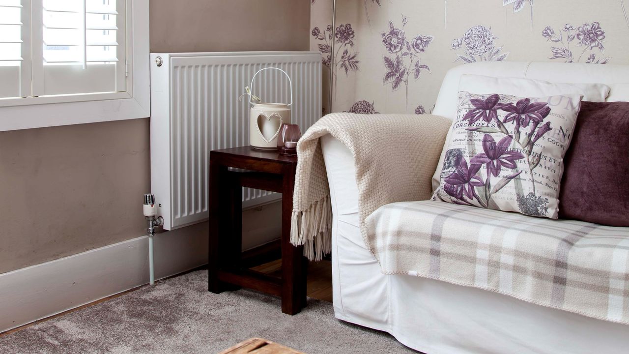 A living room with a white sofa and cushions and a radiator in the corner