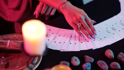 Tarotscope November 2022: Closeup image of fortune teller predicting fate with tarot cards in dark room with burning candles