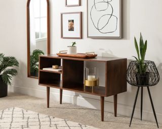 A modern entryway with arched wooden mirror, wooden console table, planter, wall art and contemporary area rug