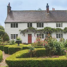 Exterior of white clapboard cottage with box hedges in front garden