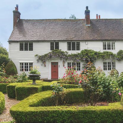 Exterior of white clapboard cottage with box hedges in front garden