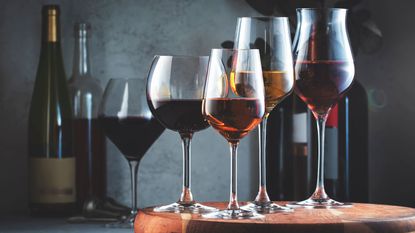 Examples of the best wine glasses - five wine glasses filled with different types of tine in front of wine bottles