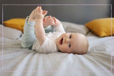 Baby rolling on bed with feet in hands