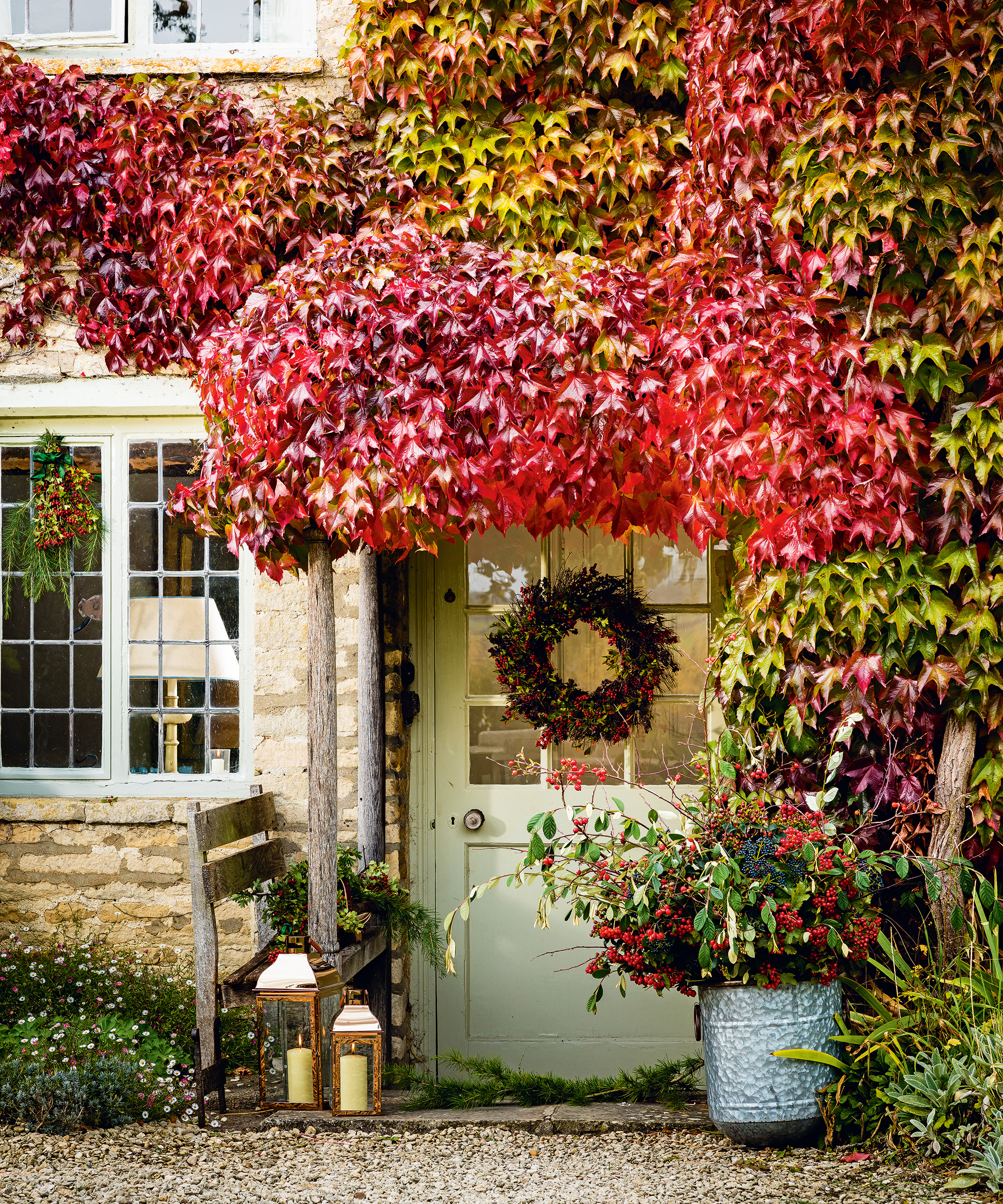 A front porch with red and green foliage over the doorway and a wreath on the door