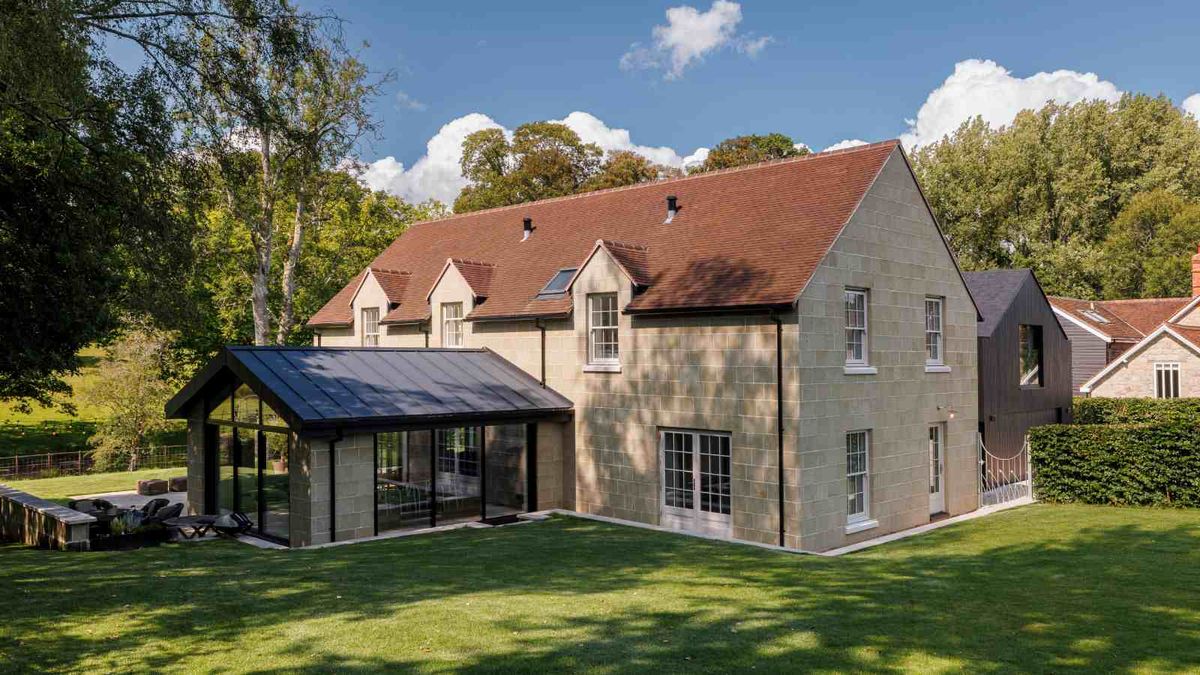 A large stone-clad new build with contemporary sunroom and clay roof tiles. The house sits adjacent to other new build homes in a farm complex. The house, built using BecoFormWall&#039;s ICF system, sits within a large plot of neat lawns and mature trees.