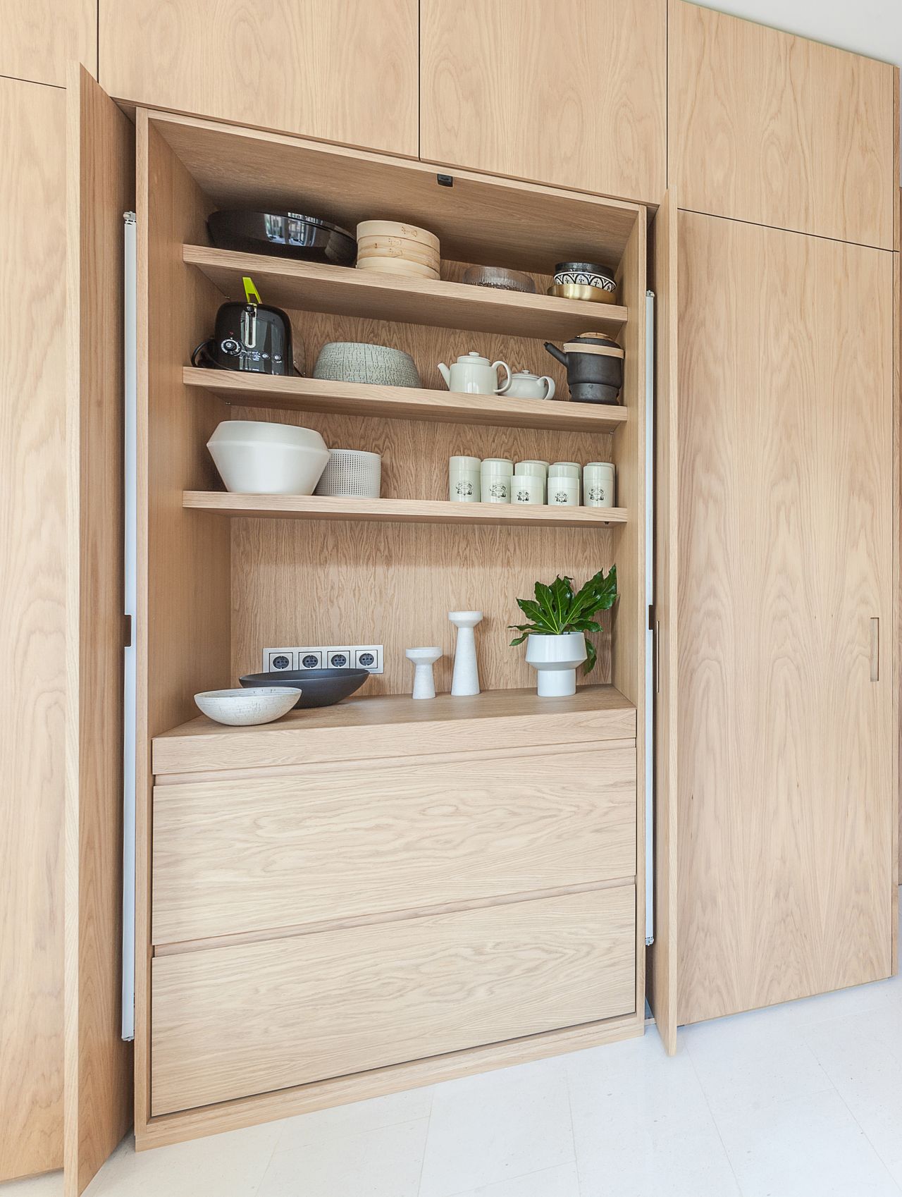 A kitchen with wooden cabinets that hide the kitchen, and a sliding door that reveals storage