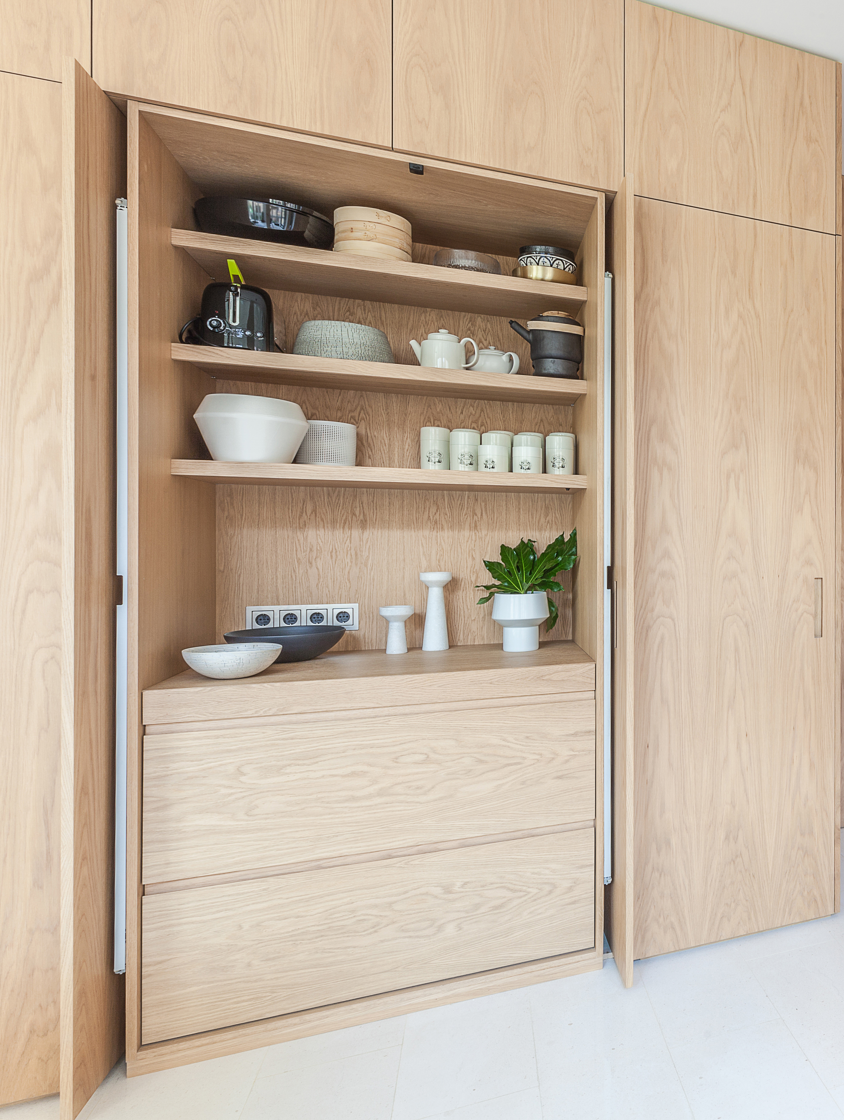 A kitchen with wooden cabinets that hide the kitchen, and a sliding door that reveals storage