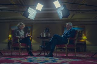 two people (Gillian Anderson as Emily Maitlis and Rufus Sewell as Prince Andrew) sit across from each other while filming an interview, with bright lights above their heads, in the netflix movie 'scooped'