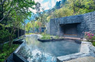 An outdoor thermal bath features brutalist style architecture surrounded by nature.