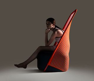 A woman sitting in a chair made with a red and white mesh back, and a deep, navy blue seat