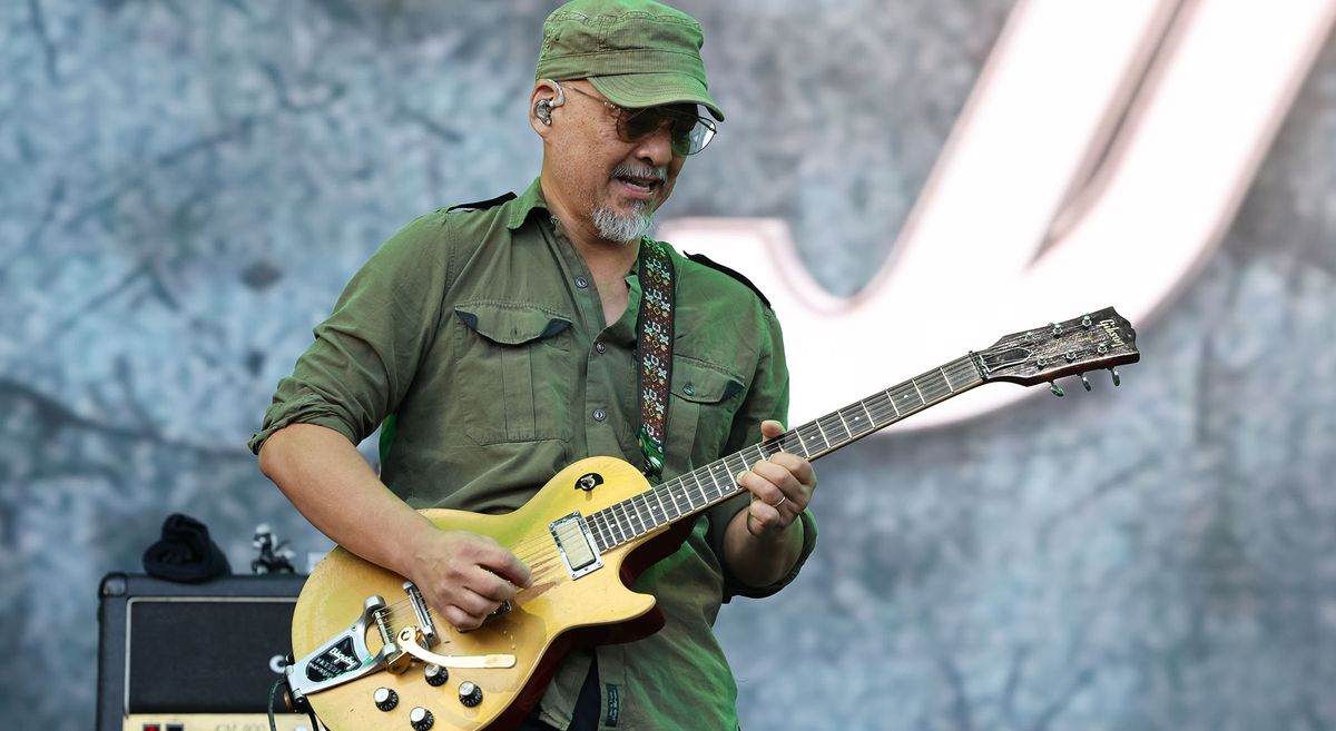 Joey Santiago of the Pixies plays his Bigsby-equipped Les Paul Goldtop live onstage. He wears an army shirt and cap.