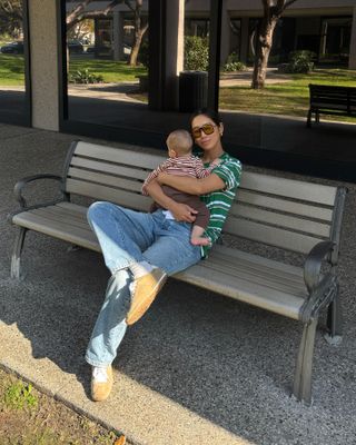 Fashion influencer @aimeesong sitting on a bench holding her baby, wearing a chic spring outfit with on-trend sneakers.