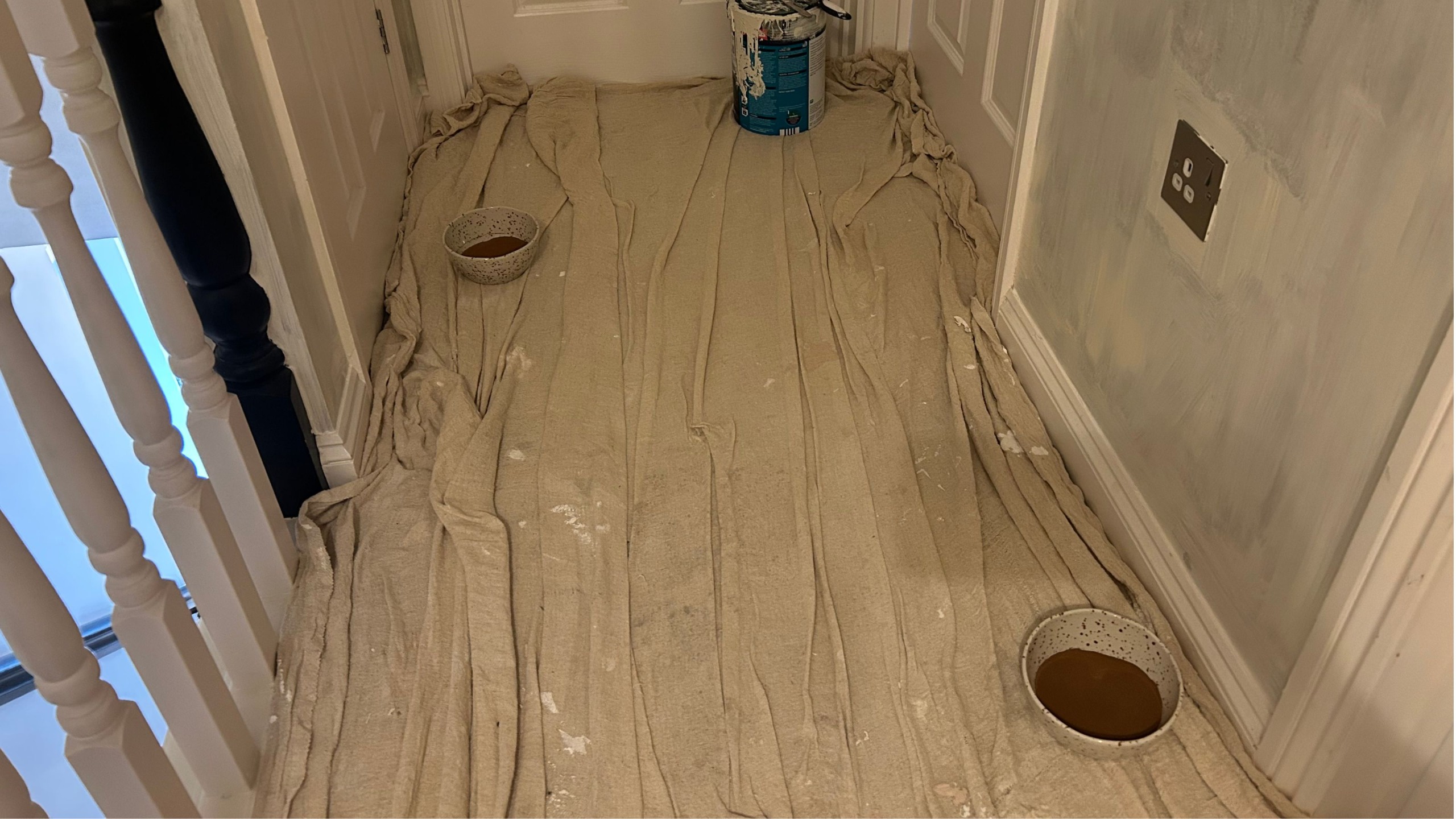 Painting a hallway with dust sheet on floor and 2 bowls of ground coffee