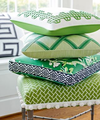 Close up of a pile of stacked green patterned cushions on a upholstered green stool with tassels