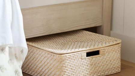 An image of a ratten under bed storage caddy peaking out from under a wooden bed frame