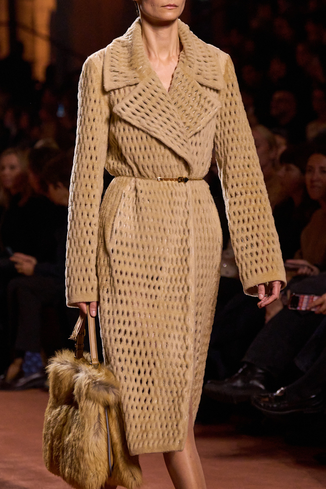 Fur accessory trend is shown in Fendi&#039;s fall-winter 2025 collection in a close photo of a model walking down the runway wearing an open-weave fur coat styled as a dress with a slim belt layered on top that&#039;s paired with sheer tights and a structured fur handbag