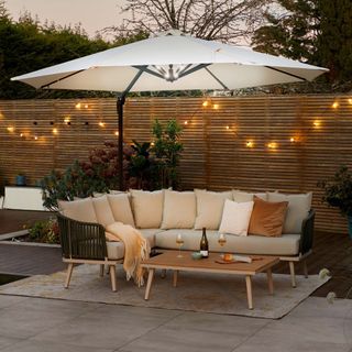 outdoor living space with parasol with LED lights underside, outdoor sofa and coffee table, fence with fairy lights