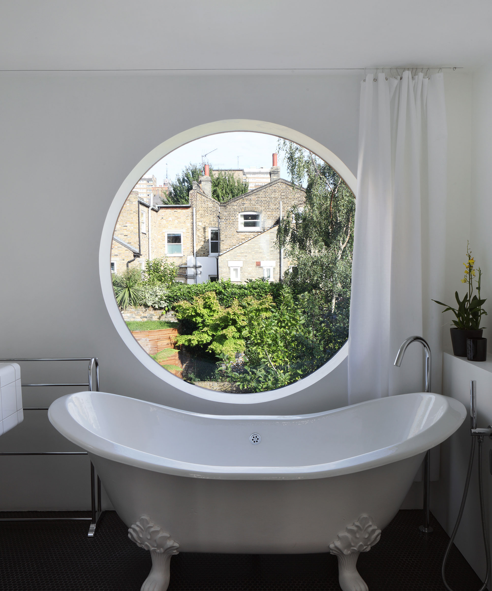 large circular window in bathroom with rolltop bath